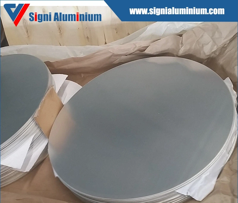 Stacks of aluminium cookware discs interleaved with paper in a packing crate